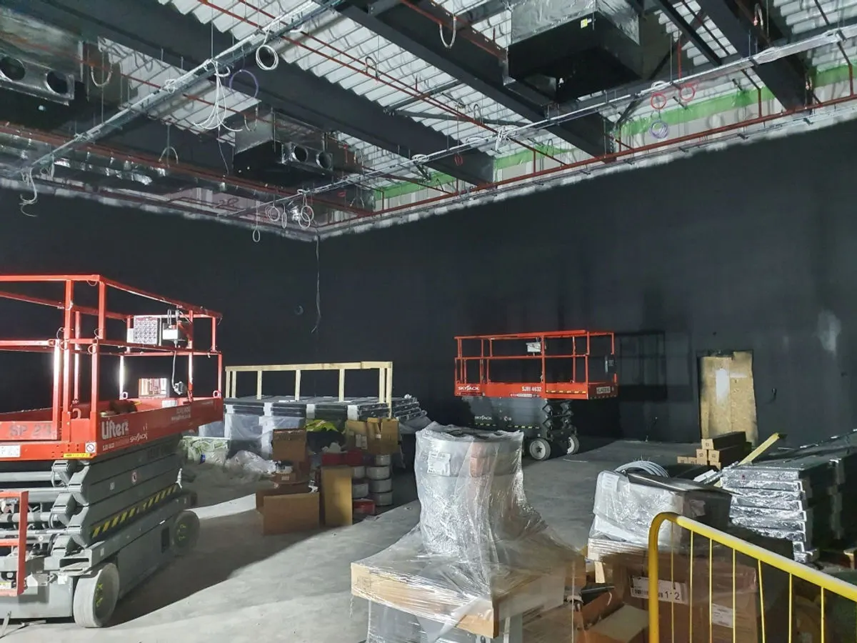 Dark-painted commercial interior with scissor lifts and construction materials stacked on floor