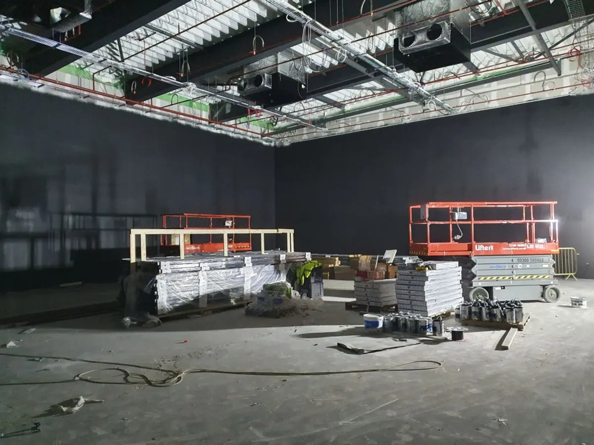 Wide angle of commercial venue with dark charcoal walls and two scissor lifts positioned for painting