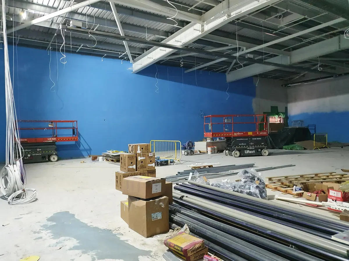 Large retail unit with bright blue feature wall being painted using scissor lifts and construction supplies