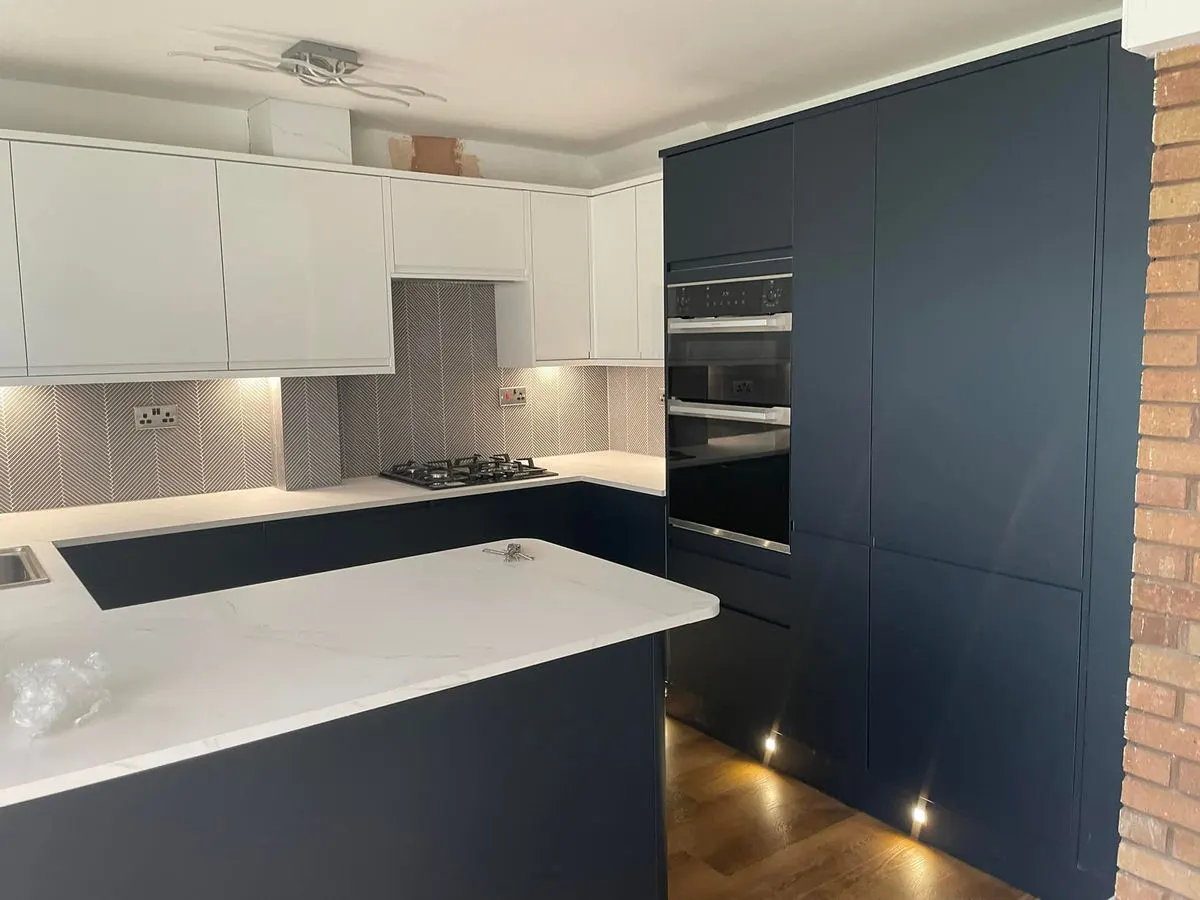 Modern kitchen with navy blue lower cabinets white uppers marble worktops and herringbone splashback
