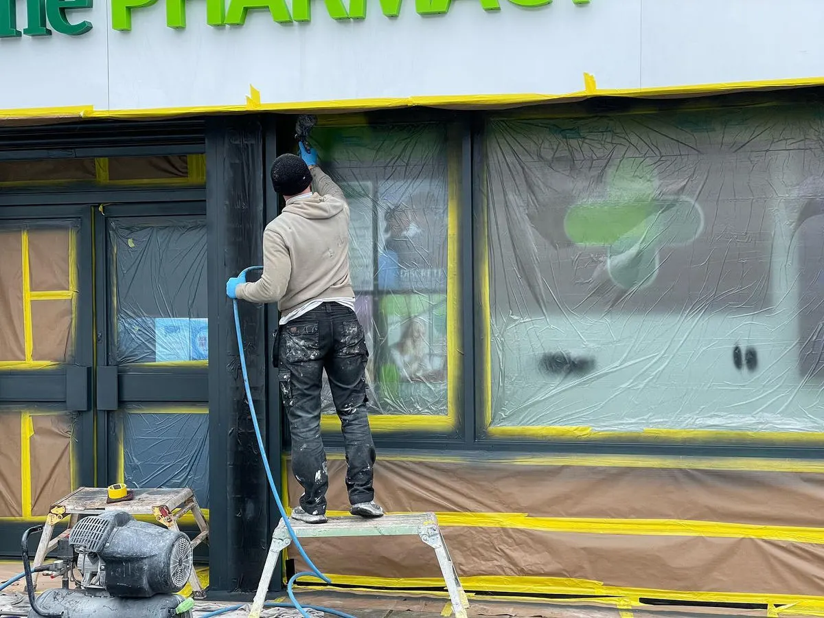 Close-up of painter spray-painting pharmacy shopfront exterior with windows and signage masked