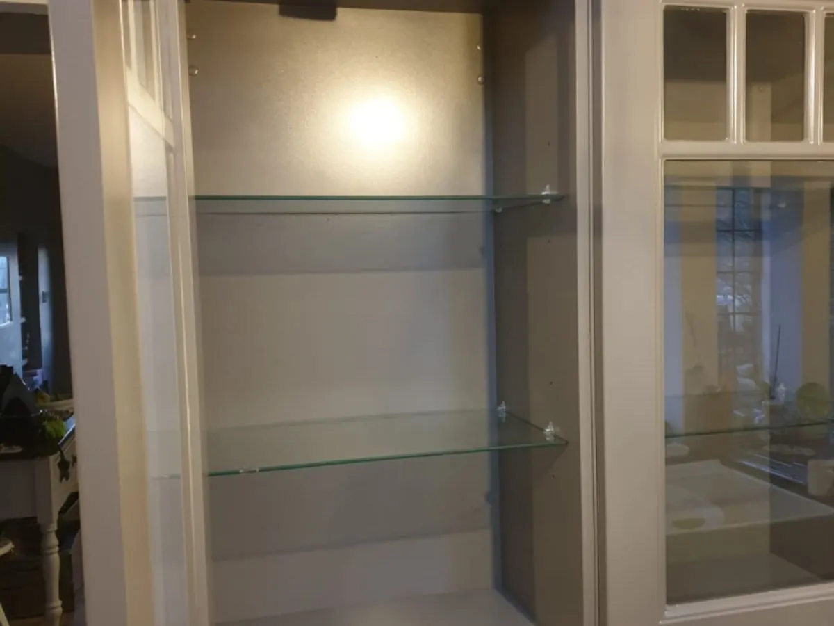 Close-up of cream sprayed glass display cabinet with internal lighting and glass shelves