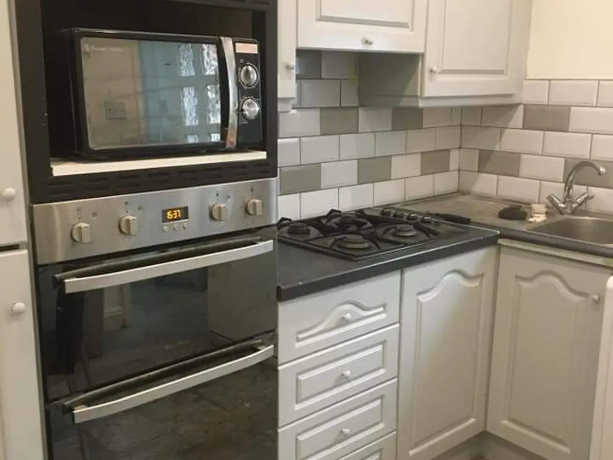 White sprayed kitchen cabinets with grey and white metro tile splashback and built-in oven