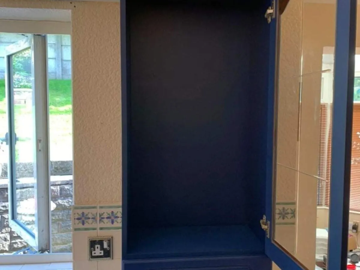 Kitchen cabinet interior sprayed in deep navy blue with mirrored door panel visible
