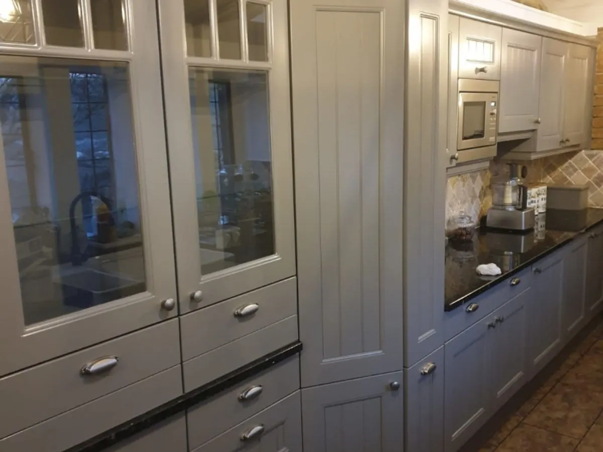Long run of grey sprayed kitchen cabinets with glass doors black granite worktop and built-in microwave