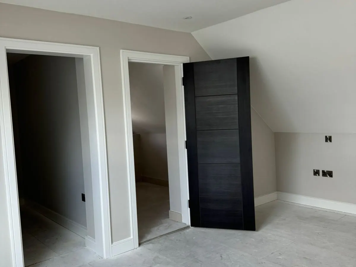Loft bedroom with freshly painted light grey walls white trim and dark contemporary internal doors