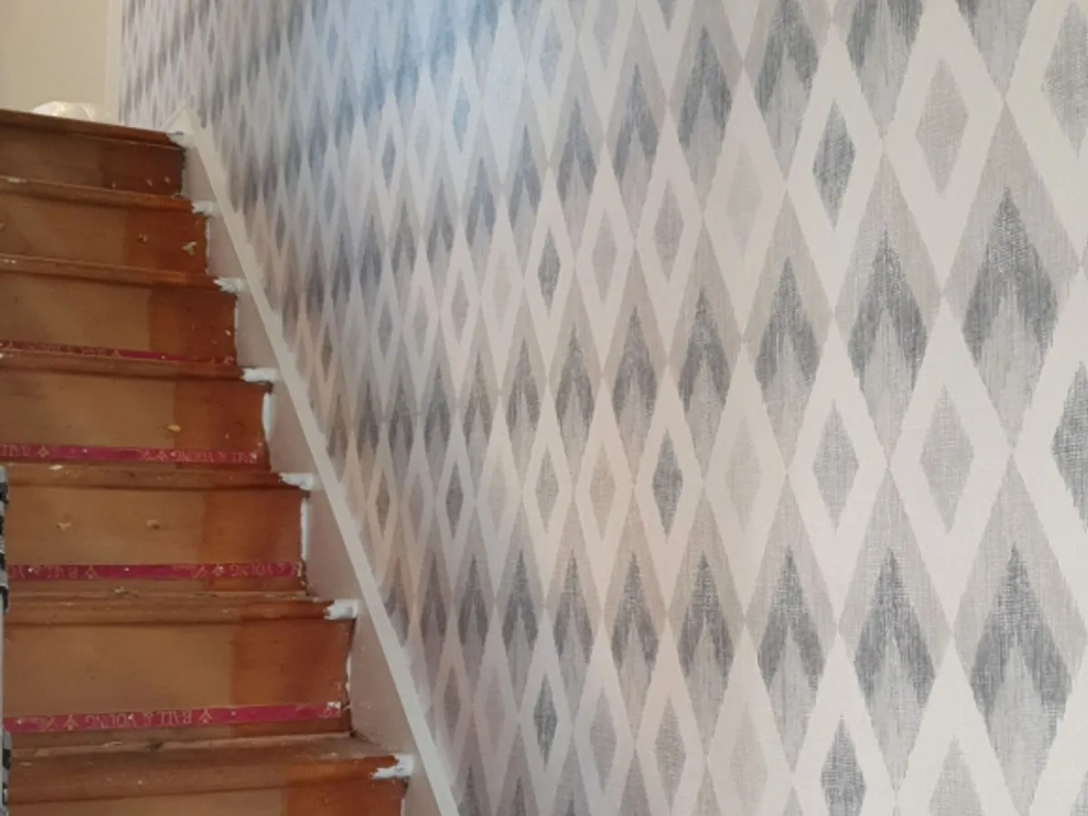 Diamond-pattern wallpaper in grey and cream neatly hung beside wooden staircase