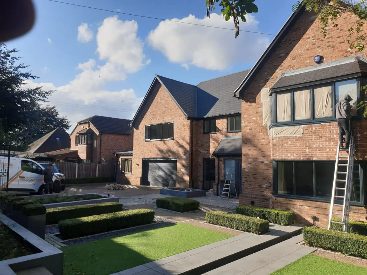 Detached brick house with grey sprayed UPVC windows being worked on with ladder and van on driveway