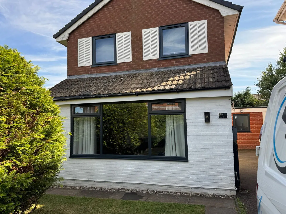 Small detached house with freshly sprayed dark grey UPVC windows and white rendered extension