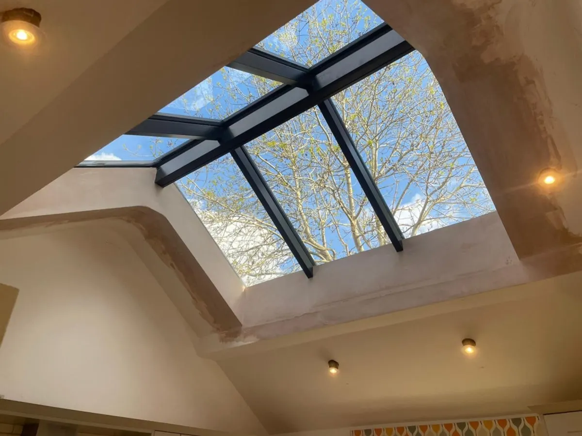 Interior view looking up at black-framed roof lantern skylight with freshly plastered ceiling surround